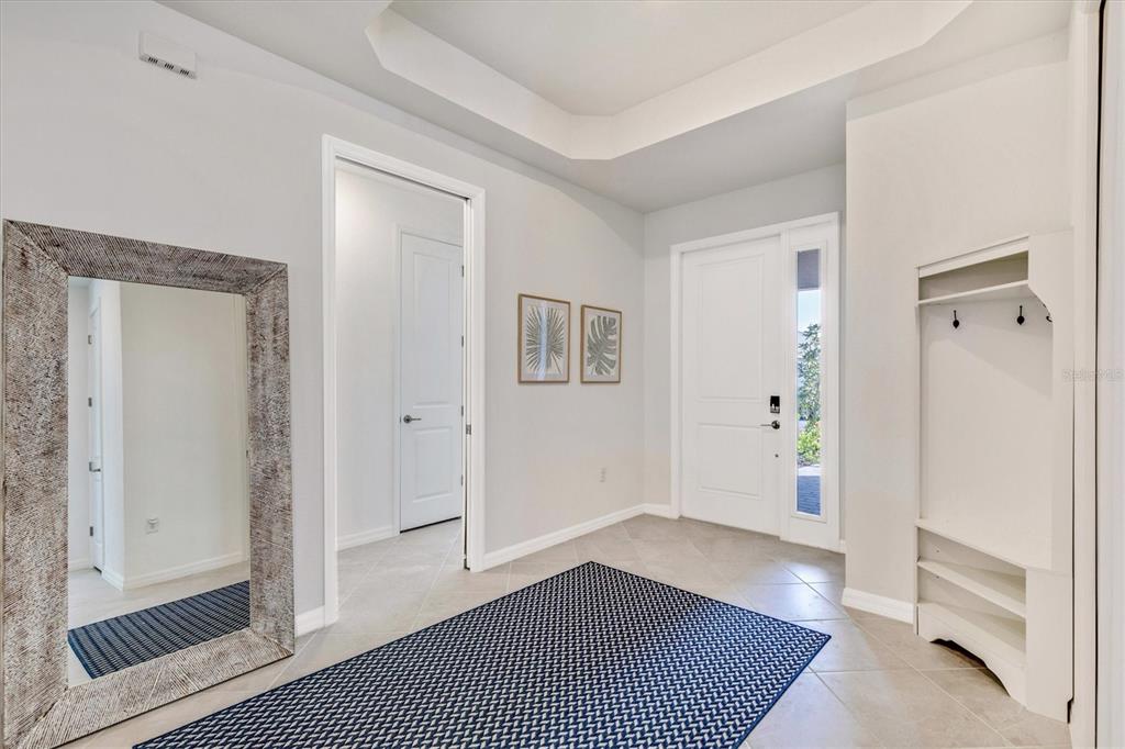 An entryway features a large floor mirror, a blue patterned rug, and a built-in coat rack — 17617 SANTORINI COURT, VENICE, FL