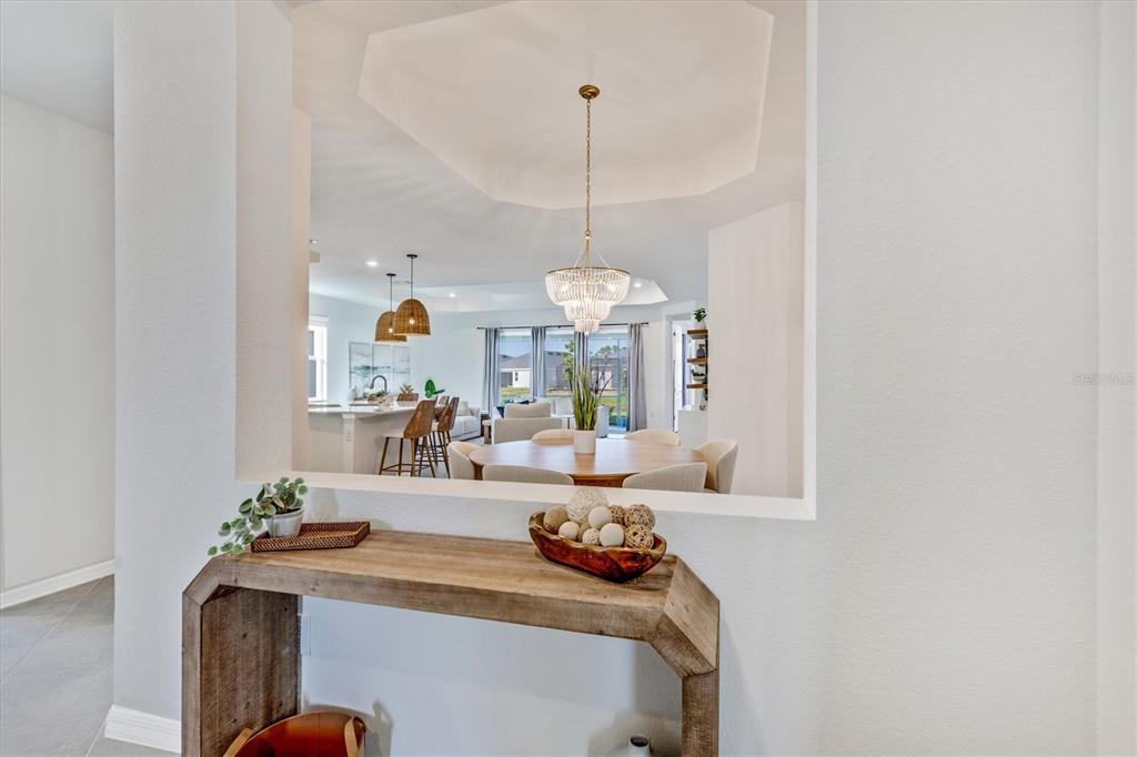 A wooden console table sits in front of a pass-through window overlooking an open-concept dining area — 17617 SANTORINI COURT, VENICE, FL