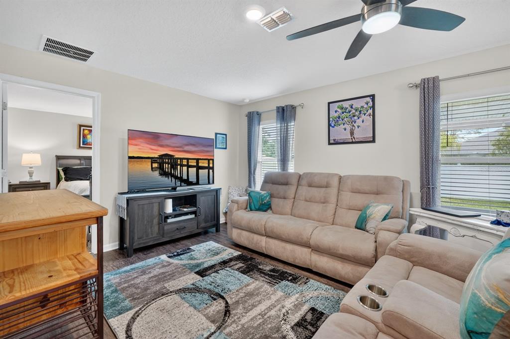 A living room features a beige reclining sofa, a television on a console, and area rug — 629 GRAND RESERVE DRIVE, BUNNELL, FL