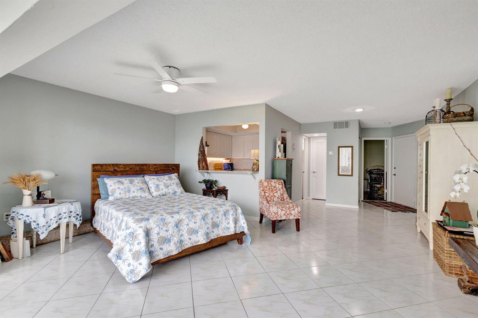 A bedroom features a wooden bed, tile flooring, a ceiling fan, and an open kitchen pass-through — 2936 Lake Shore Drive # 309, Riviera Beach FL 33404, RIVIERA BEACH, FL