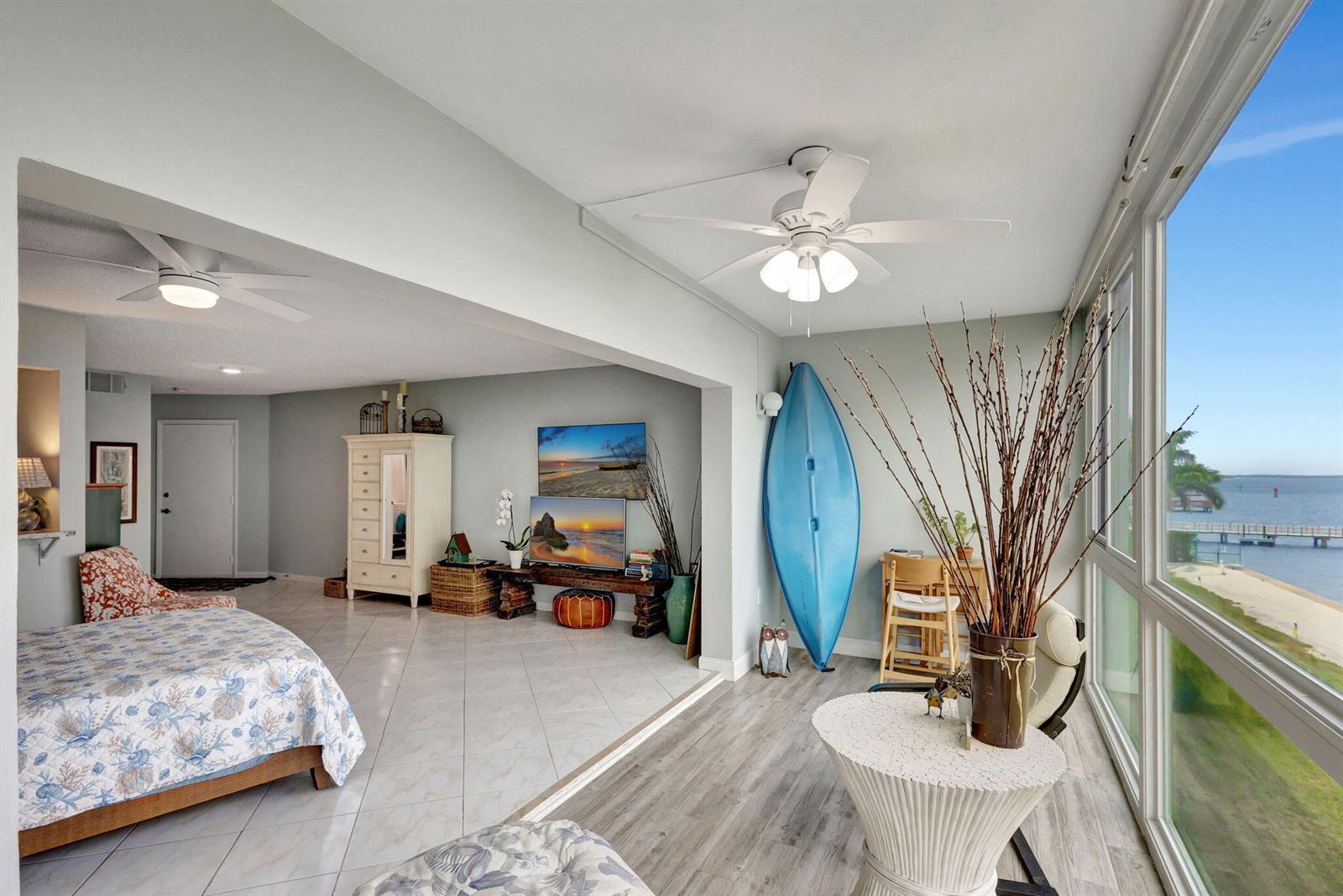 A bedroom with tile and wood-look flooring features a blue kayak and waterfront window views — 2936 Lake Shore Drive # 309, Riviera Beach FL 33404, RIVIERA BEACH, FL