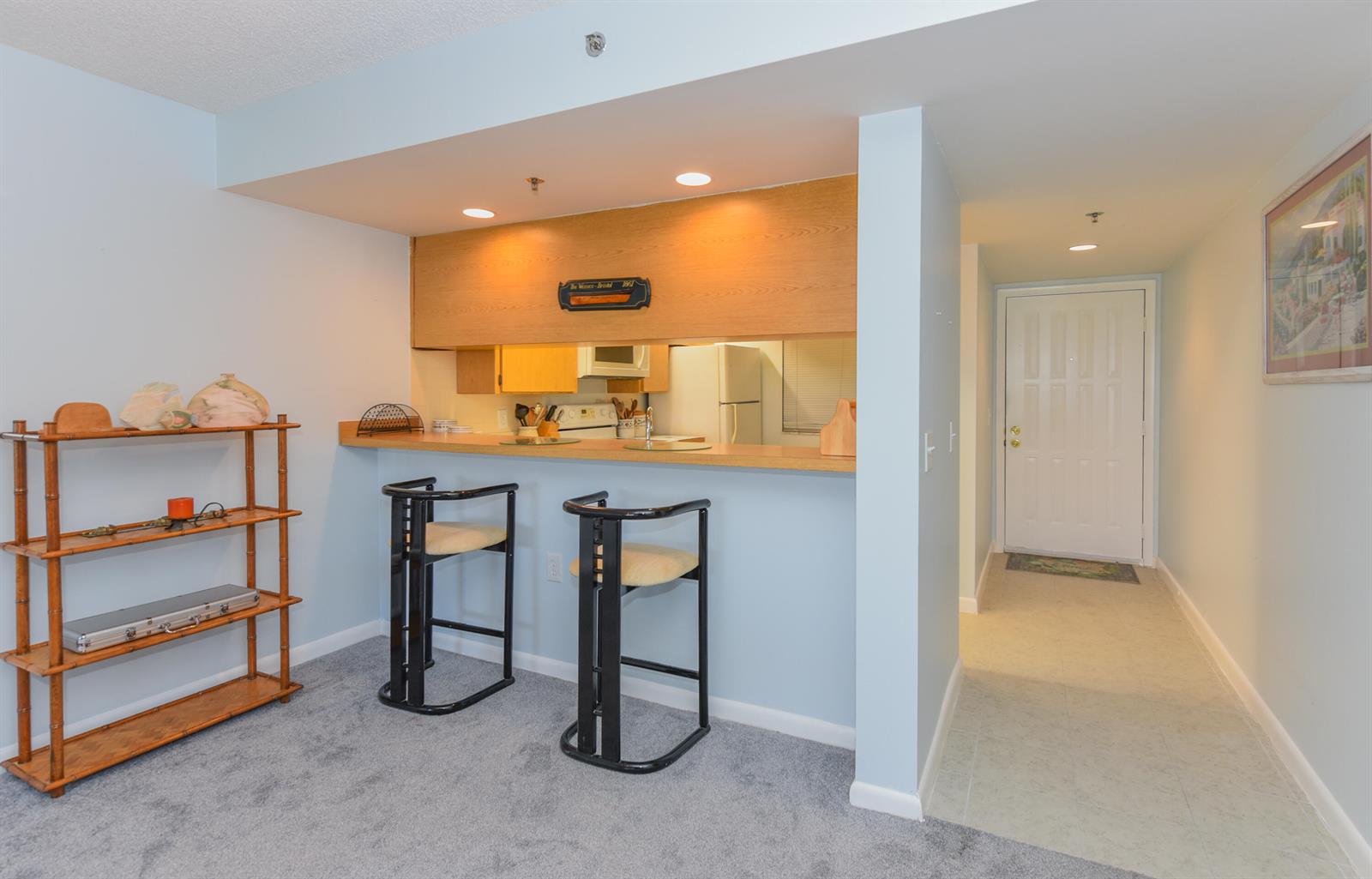 A kitchen pass-through with a breakfast bar and two stools overlooks a carpeted living area — 601 S Seas Drive # 303, Jupiter FL 33477, JUPITER, FL