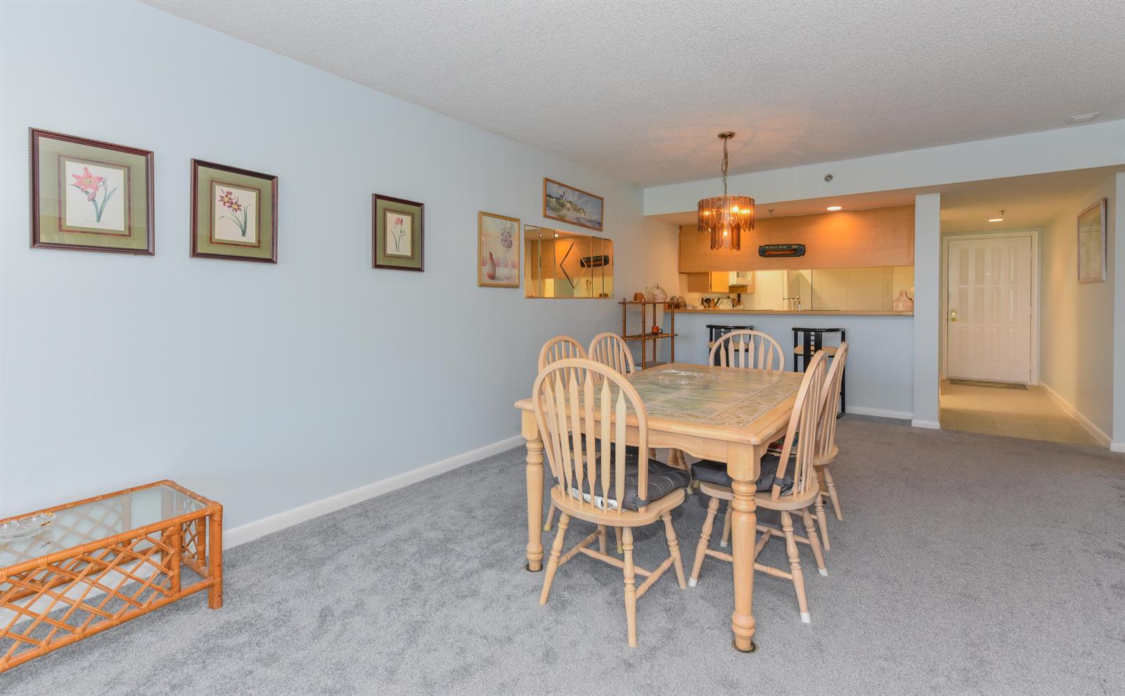 A dining area features a wooden table with chairs, carpeted flooring, and an open kitchen — 601 S Seas Drive # 303, Jupiter FL 33477, JUPITER, FL