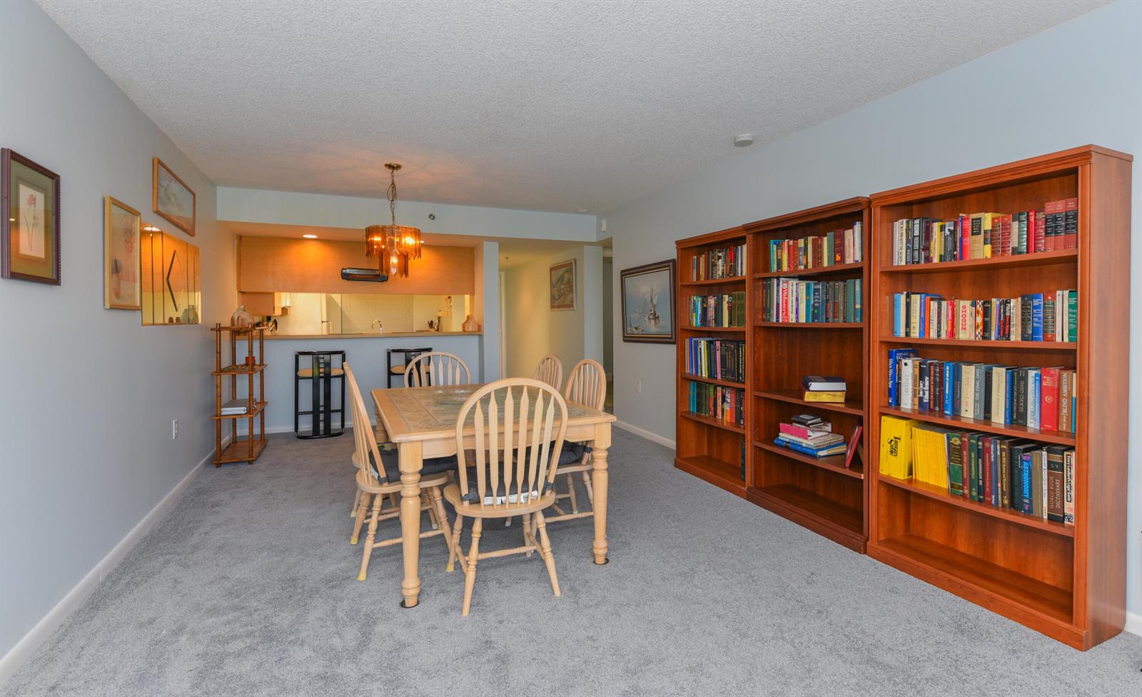 A dining area with a wooden table, chairs, and two large bookshelves on gray carpet — 601 S Seas Drive # 303, Jupiter FL 33477, JUPITER, FL