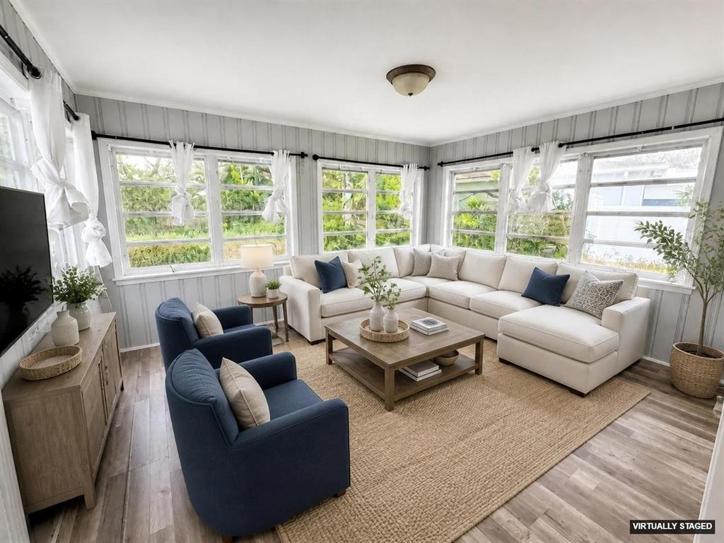 A sunroom features a sectional sofa, two blue armchairs, and large windows with vertical paneling — 309 BELLE CLAIRE PLACE, TEMPLE TERRACE, FL