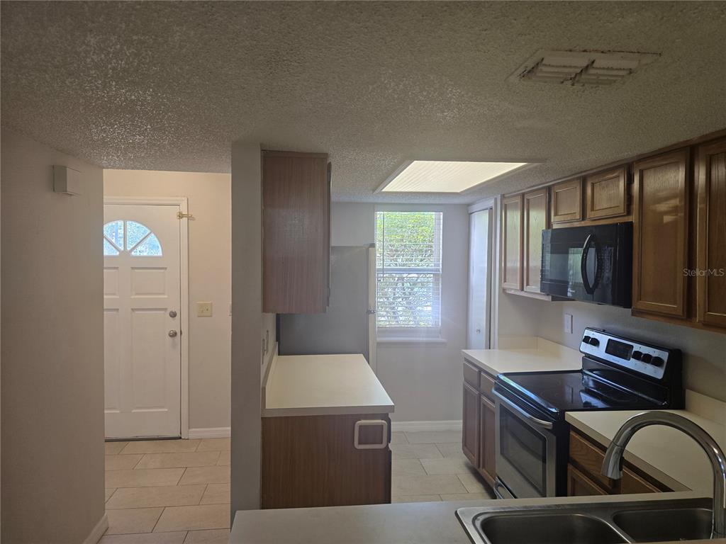 A kitchen features wood cabinets, white countertops, a black microwave, and a black stove — 8713 LIBERTY PLACE, TAMPA, FL