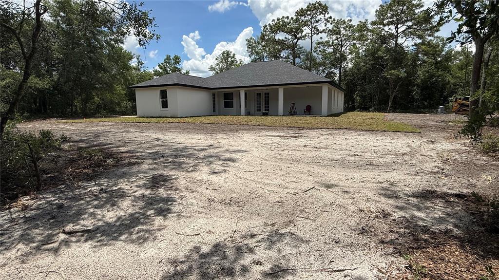 A white single-story house with a covered patio sits on a large, sandy lot — 35031 PRIMROSE LANE, WEBSTER, FL