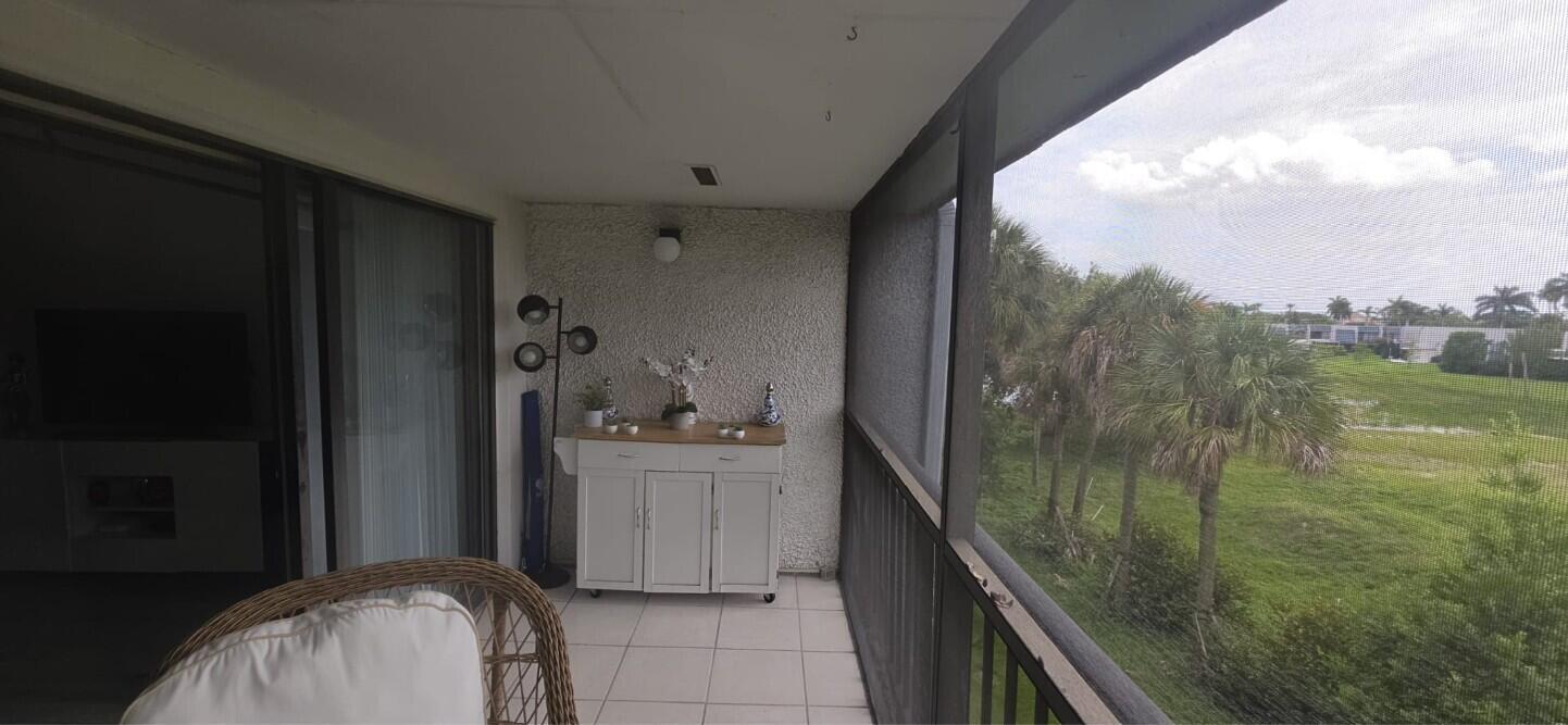 A screened-in balcony features white tile flooring, a white cabinet, and a view of trees — 4284 Deste # 304, Lake Worth FL 33467, LAKE WORTH, FL