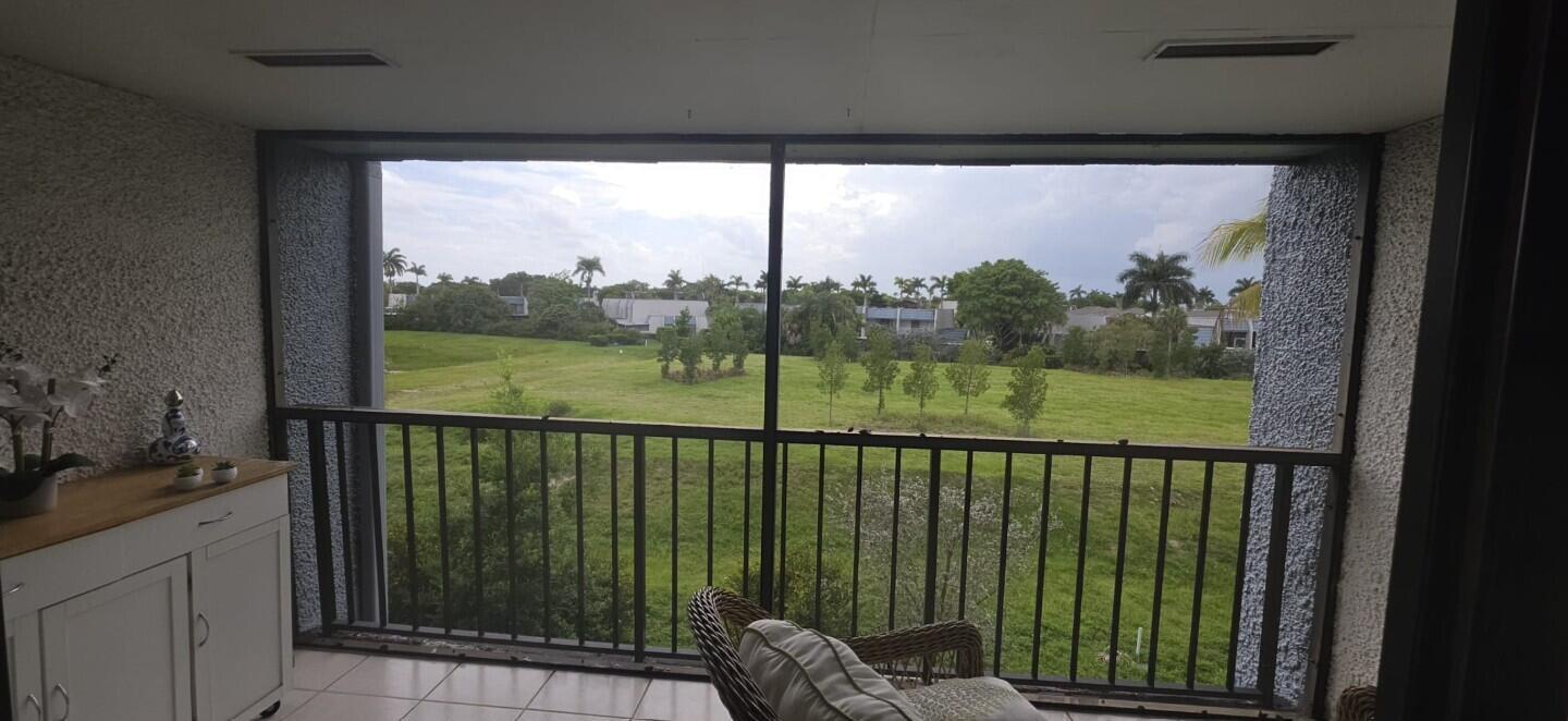A screened-in balcony overlooks a grassy field with trees and distant residential buildings — 4284 Deste # 304, Lake Worth FL 33467, LAKE WORTH, FL
