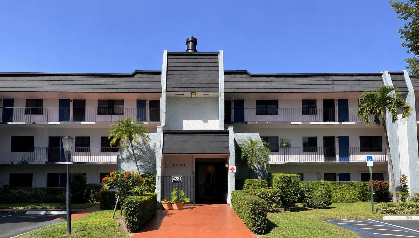 A three-story apartment building with a central entrance, dark roof, and surrounding landscaping — 4284 Deste # 304, Lake Worth FL 33467, LAKE WORTH, FL