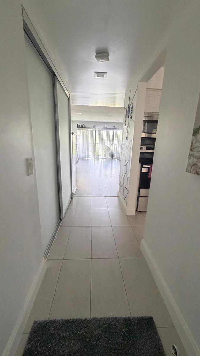 A tiled hallway leads to a living area with sliding glass doors and a kitchen — 4284 Deste # 304, Lake Worth FL 33467, LAKE WORTH, FL