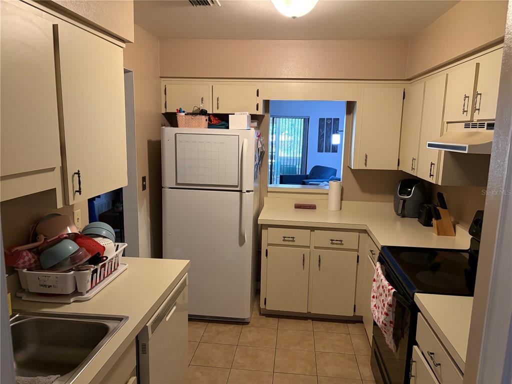 A kitchen features beige cabinets, white appliances, a tiled floor, and a pass-through window — 821 SLEEPY HARBOUR DRIVE, OCOEE, FL