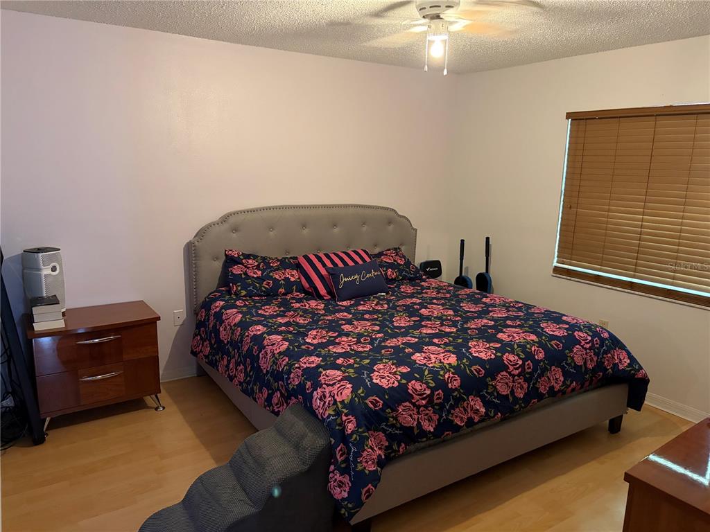 A bedroom features a tufted headboard, floral bedding, wood flooring, and a ceiling fan — 821 SLEEPY HARBOUR DRIVE, OCOEE, FL