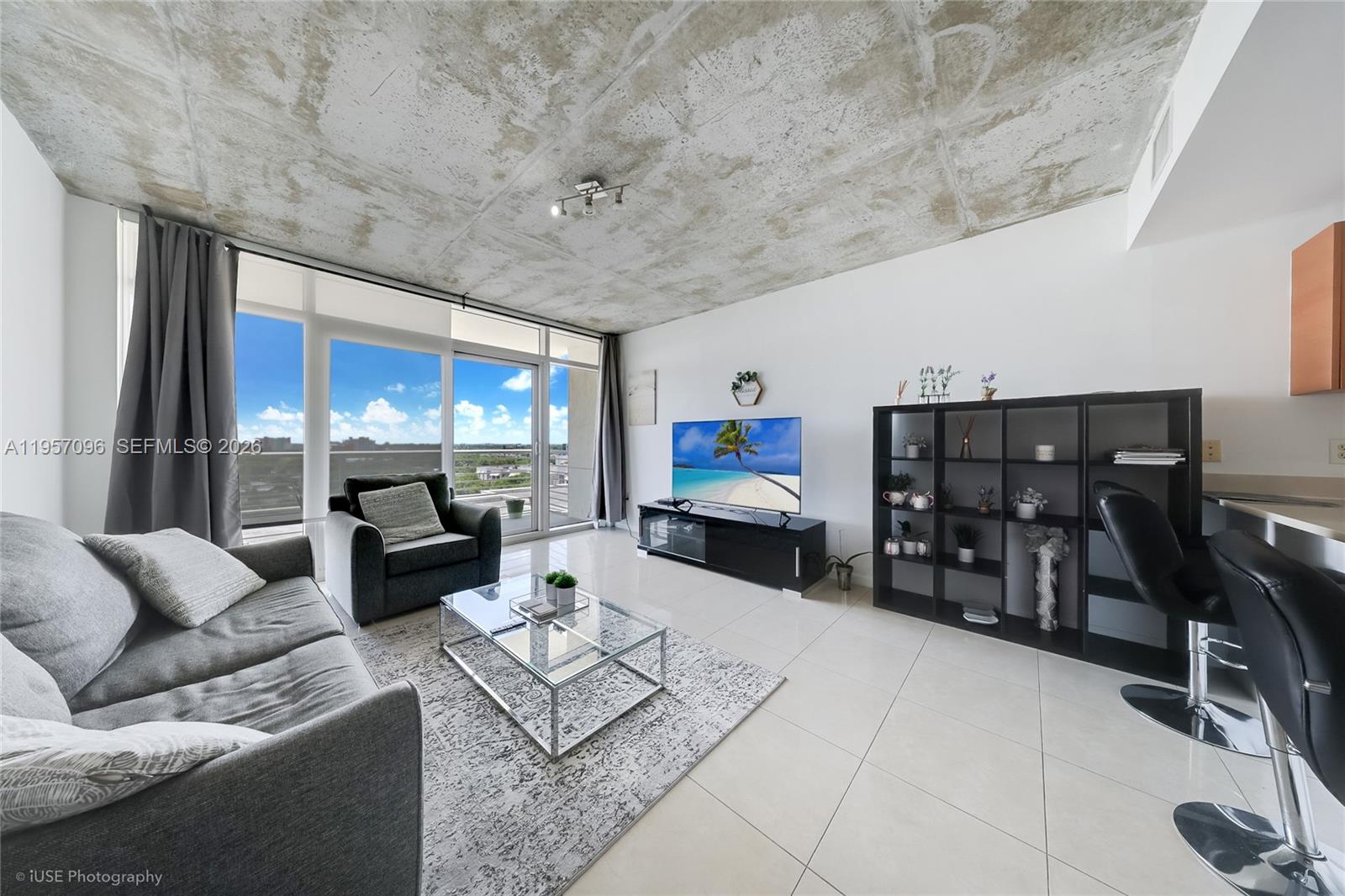 A living room features a concrete ceiling, tiled floors, a glass coffee table, and balcony access — 3250 NE 1st Ave # 811, Miami FL 33137, MIAMI, FL