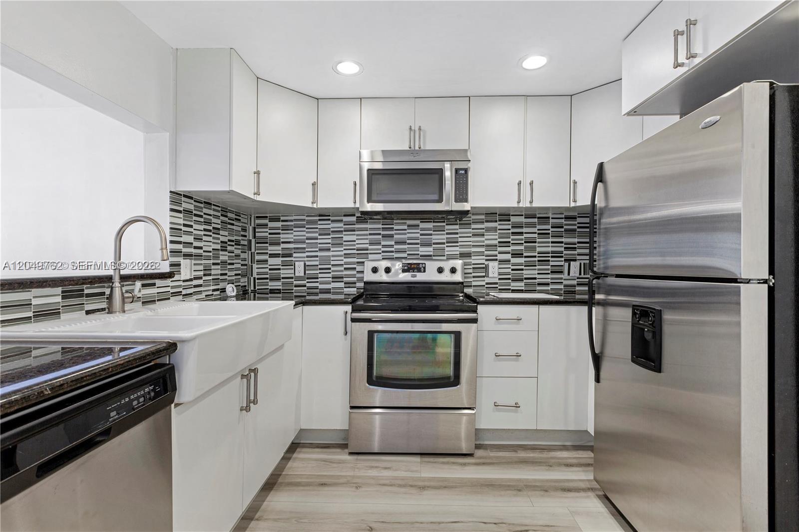 A kitchen features white cabinets, stainless steel appliances, a farmhouse sink, and a patterned backsplash — 11219 SW 88th St # C208, Miami FL 33176, MIAMI, FL