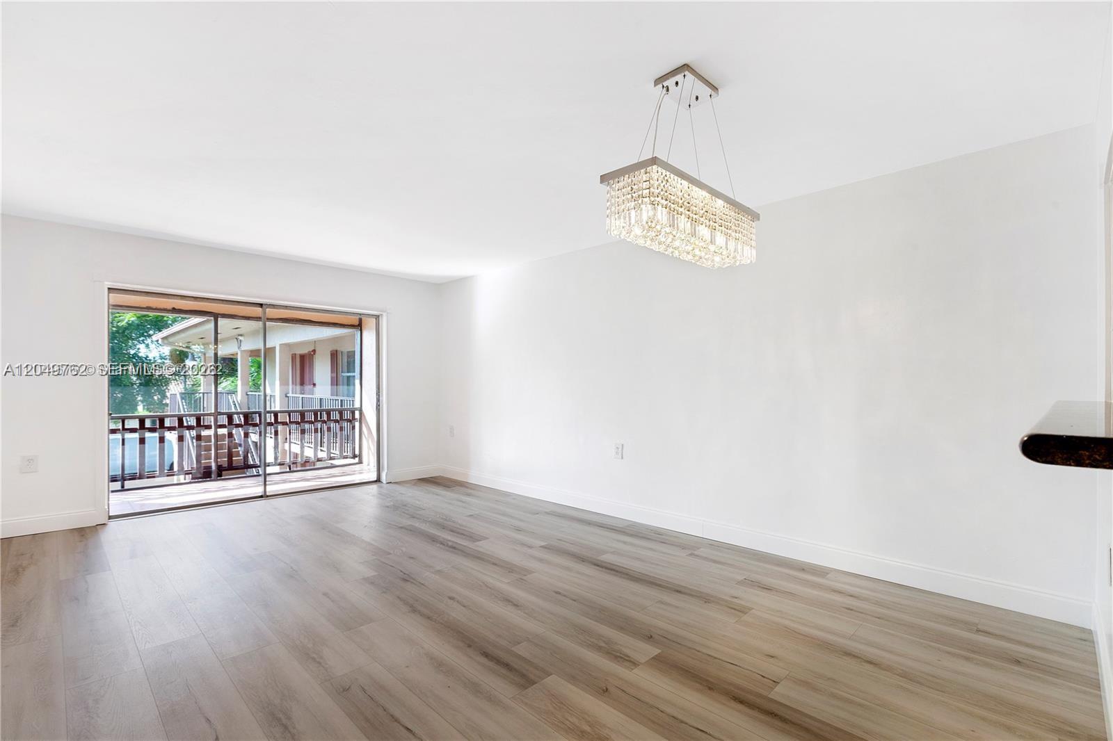 A bright living room features light wood-look flooring, white walls, and a rectangular crystal chandelier — 11219 SW 88th St # C208, Miami FL 33176, MIAMI, FL
