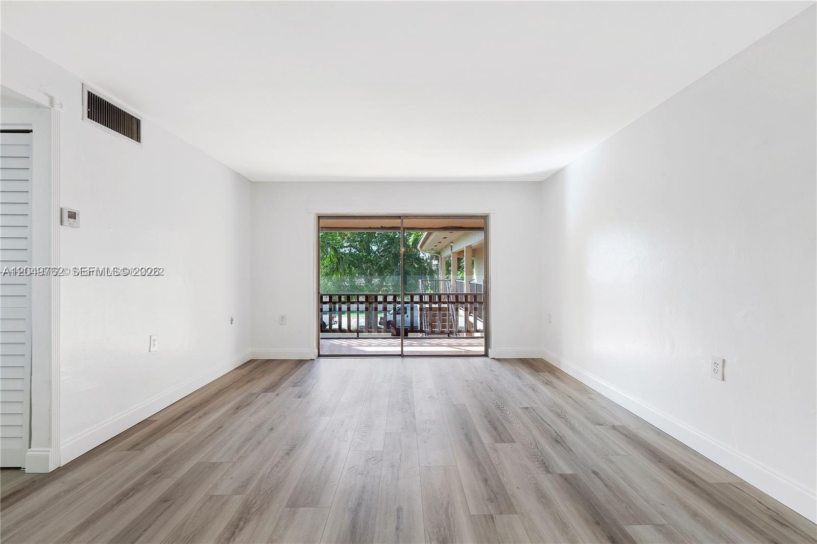 An empty room features white walls, wood-look flooring, and a sliding glass door to a balcony — 11219 SW 88th St # C208, Miami FL 33176, MIAMI, FL