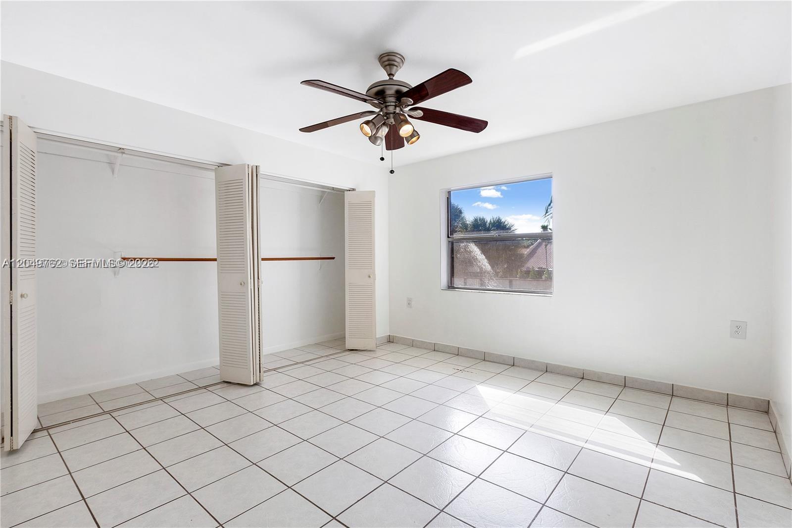 An empty bedroom features white walls, tile flooring, a ceiling fan, and a double closet — 11219 SW 88th St # C208, Miami FL 33176, MIAMI, FL