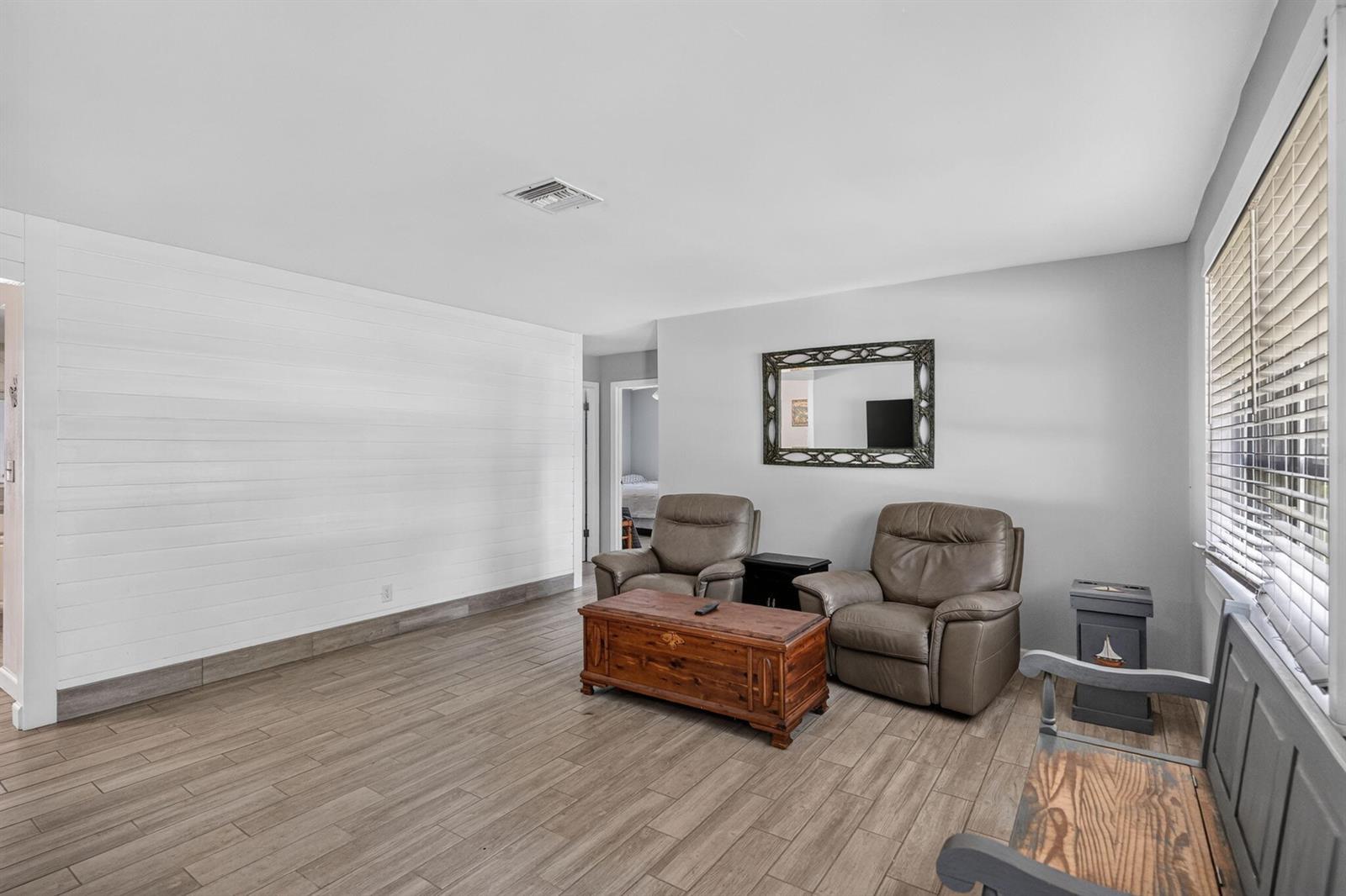 A living room features wood-look tile flooring, a white shiplap wall, and two leather recliners — 17751 127th Drive N, Jupiter FL 33478, JUPITER, FL