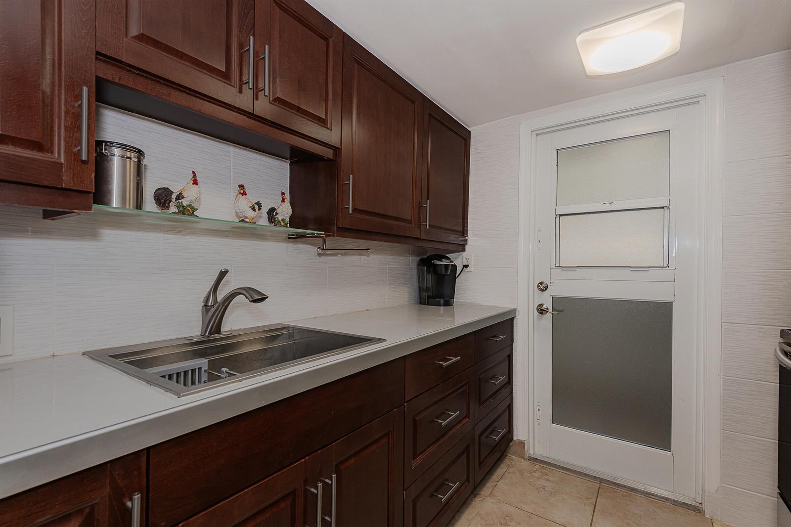 A kitchen features dark wood cabinets, a stainless steel sink, and a white exterior door — 2076 S Ocean Drive # 207, Hallandale Beach FL 33009, HALLANDALE BEACH, FL