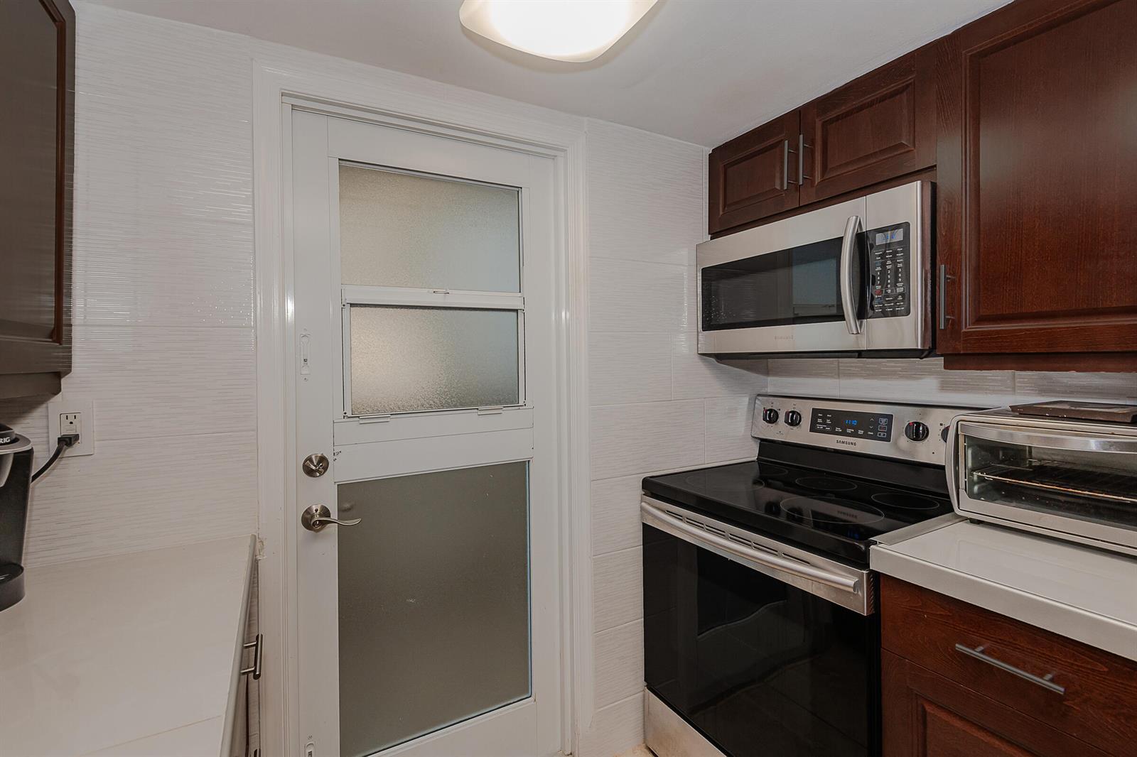 A kitchen features dark wood cabinets, stainless steel appliances, and a white door with glass — 2076 S Ocean Drive # 207, Hallandale Beach FL 33009, HALLANDALE BEACH, FL