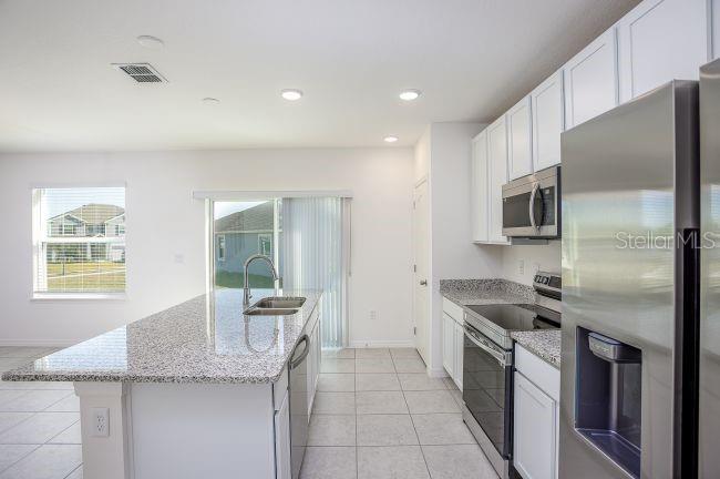 A modern kitchen features white cabinets, granite countertops, a center island, and stainless steel appliances — 8099 SW 9TH LANE, GAINESVILLE, FL