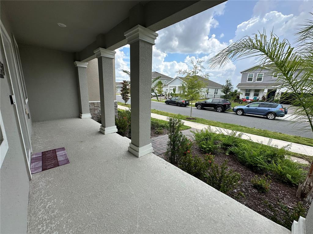 A covered concrete front porch features square columns and a view of a suburban street — 3037 ELLA WAY, ST CLOUD, FL