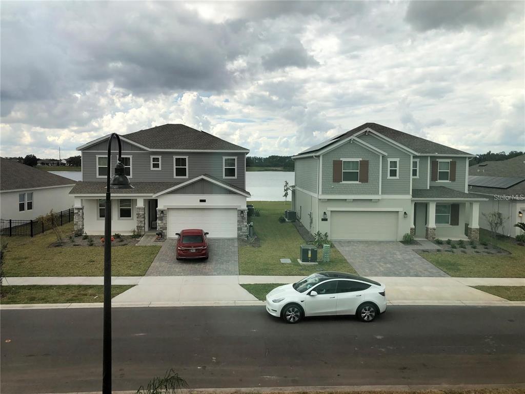 Two suburban houses with driveways and a white car face a lake under a cloudy sky — 3037 ELLA WAY, ST CLOUD, FL