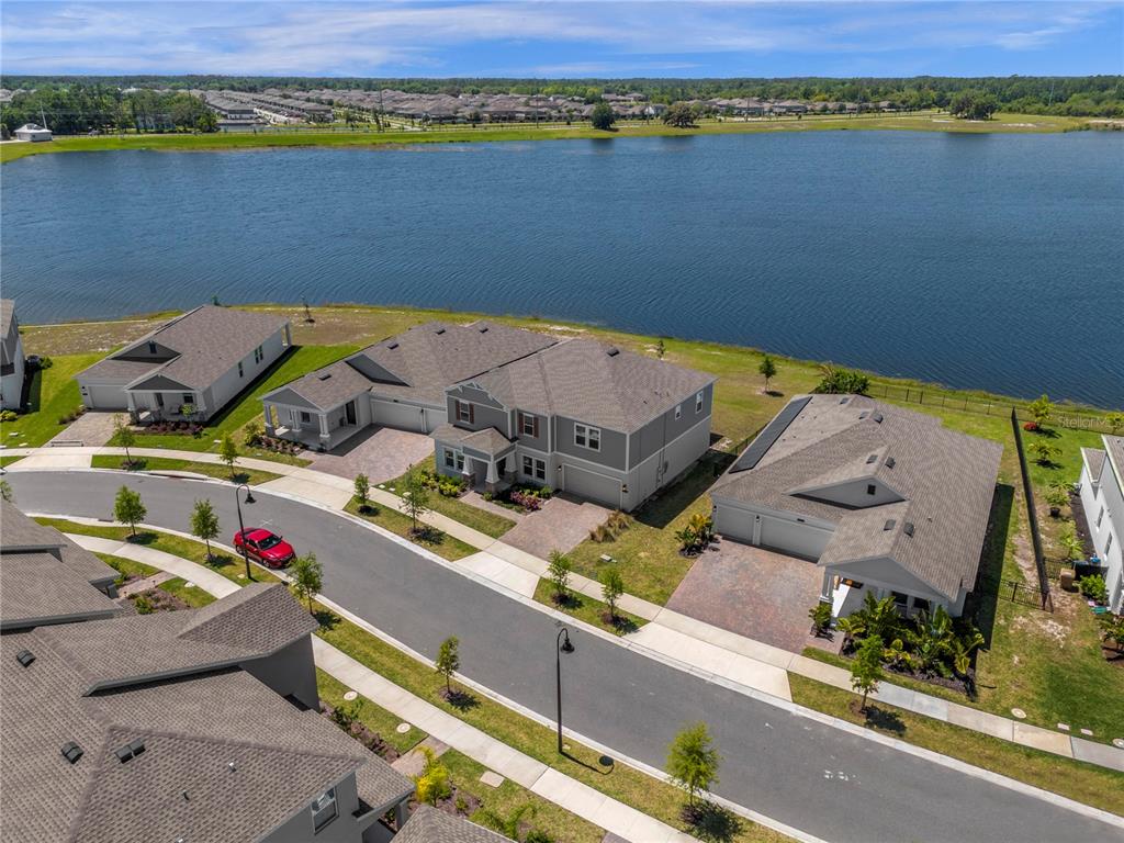 An aerial view shows several suburban houses situated along a lake with a paved street — 3037 ELLA WAY, ST CLOUD, FL