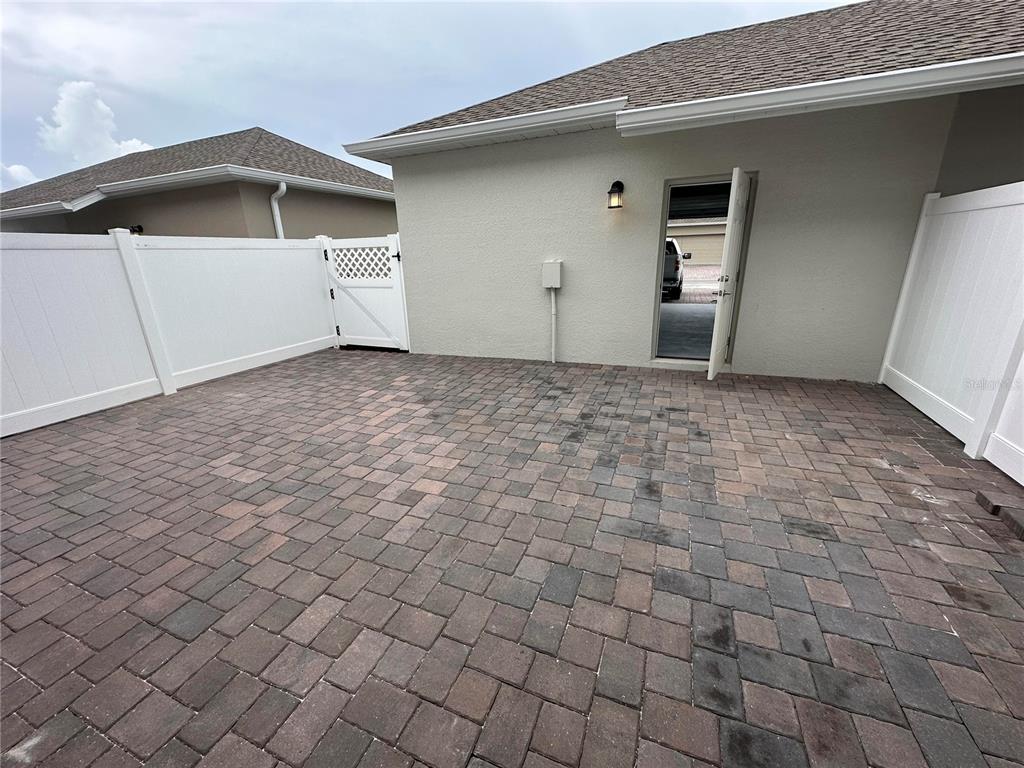 A paved patio area features a white vinyl fence and an open door to a garage — 3037 ELLA WAY, ST CLOUD, FL