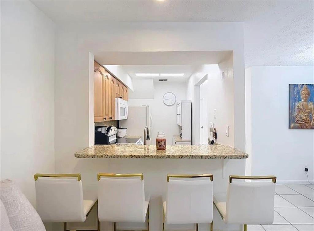 A kitchen with wood cabinets and a granite breakfast bar featuring four white chairs — 10131 LAKE OAK CIRCLE, TAMPA, FL
