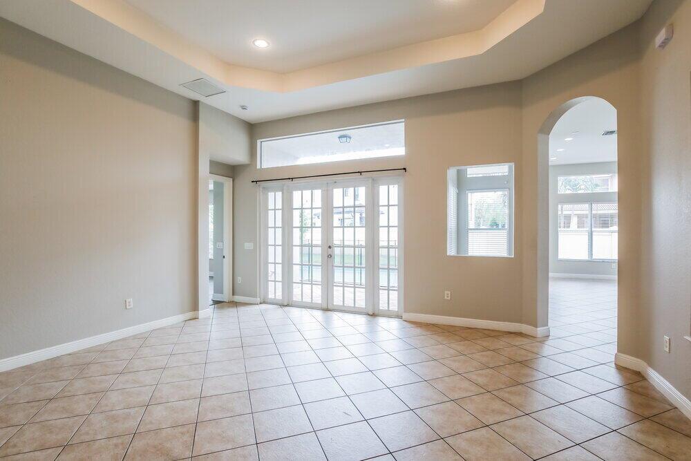 An empty room with beige walls, tile flooring, a tray ceiling, and glass French doors — MIRAMAR, FL