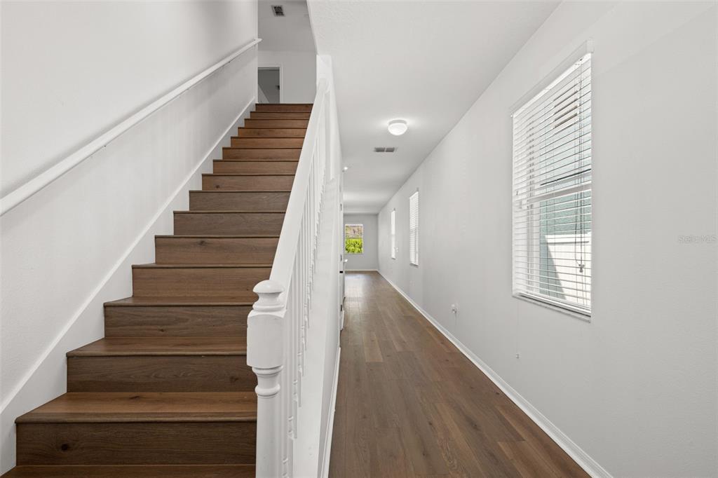 A hallway with wood-look flooring leads to a staircase with dark wood treads — 18928 HAMPSTEAD HEATH COURT, LAND O LAKES, FL
