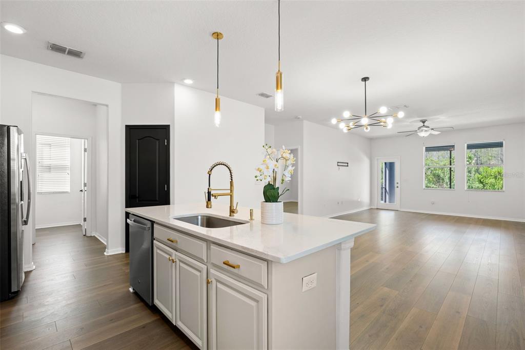 A kitchen island with a sink and gold faucet sits in a bright open-concept room — 18928 HAMPSTEAD HEATH COURT, LAND O LAKES, FL