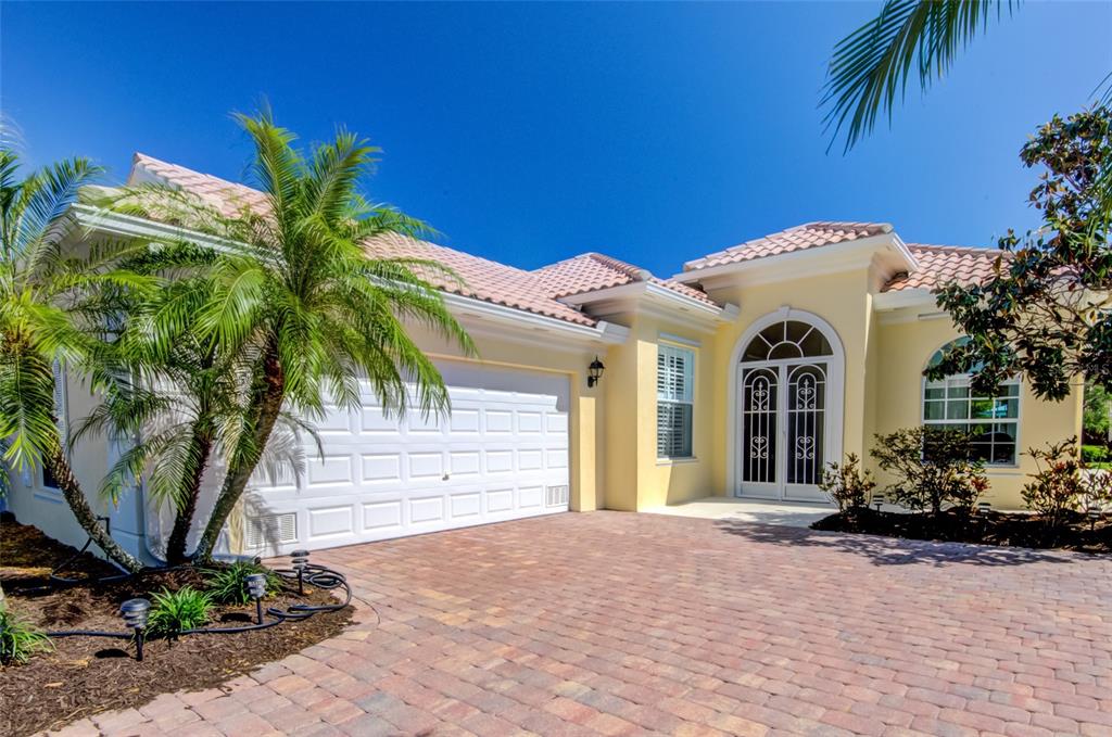 A yellow house with a tiled roof, a two-car garage, and a brick paver driveway — 5622 OCTONIA PLACE, SARASOTA, FL