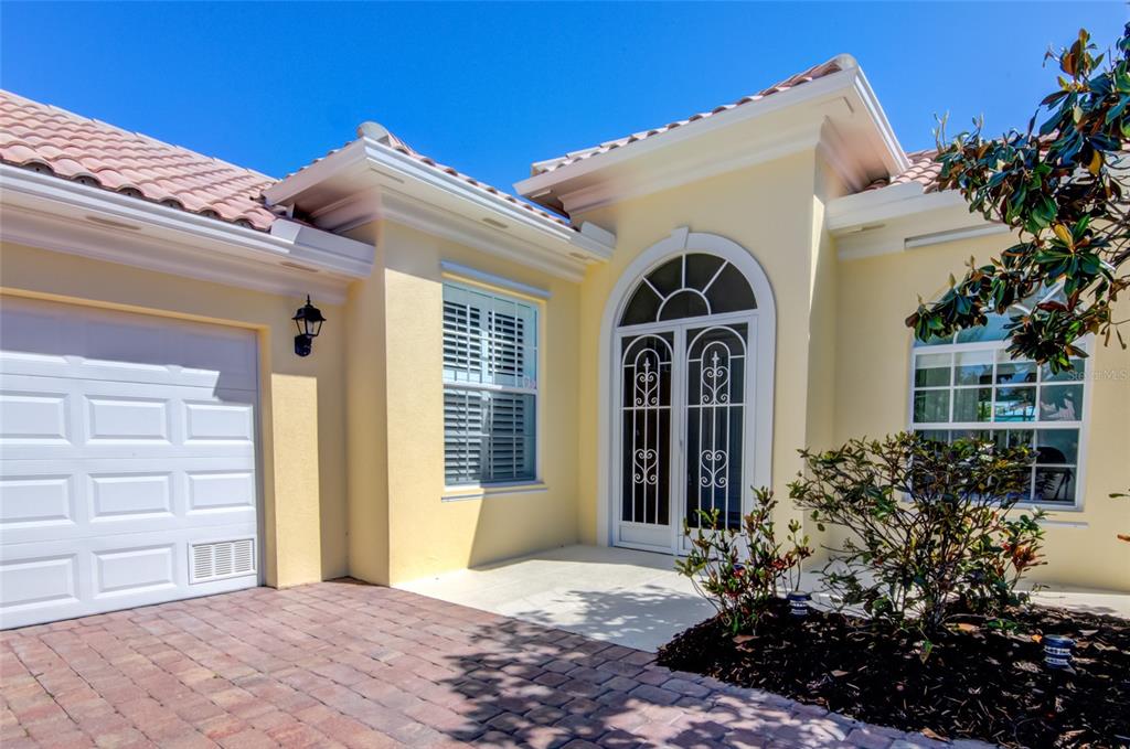 A light yellow house exterior features a white garage door, arched entryway, and paved driveway — 5622 OCTONIA PLACE, SARASOTA, FL