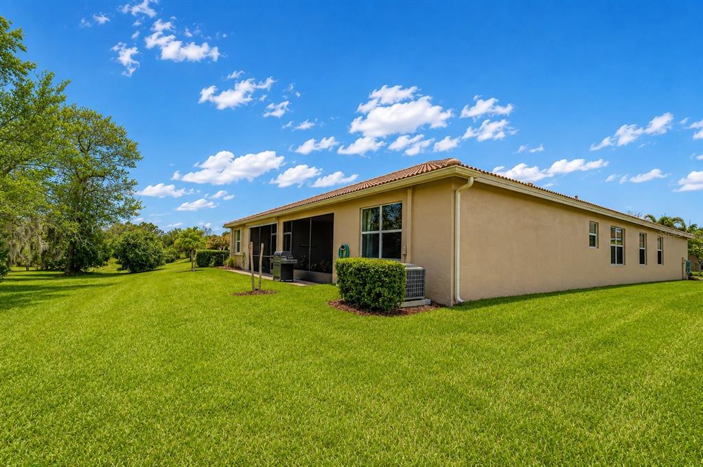 The exterior of a tan stucco house with a screened-in patio and a large lawn — 16158 AMETHYST KEY DRIVE, WIMAUMA, FL
