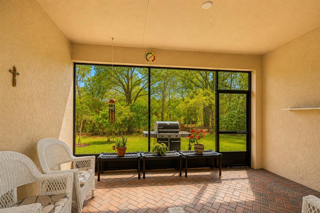 A screened-in patio with brick flooring, wicker furniture, and a view of a wooded backyard — 16158 AMETHYST KEY DRIVE, WIMAUMA, FL