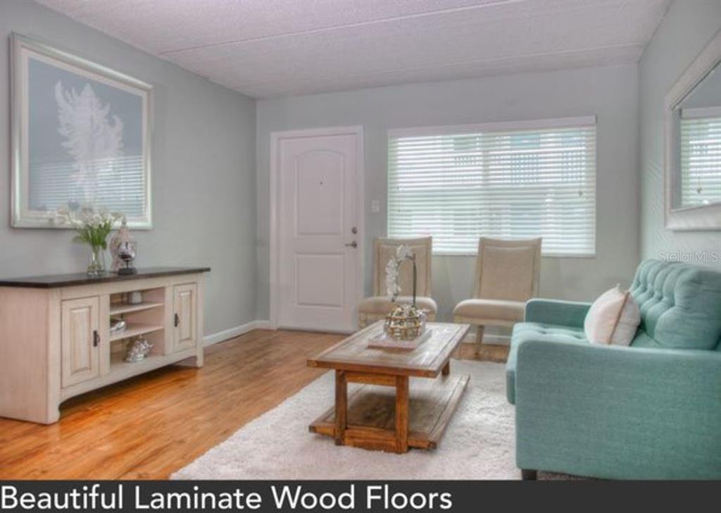 A living room features light gray walls, laminate wood floors, a teal sofa, and furniture — 1824 SHORE DRIVE S UNIT 201, SOUTH PASADENA, FL