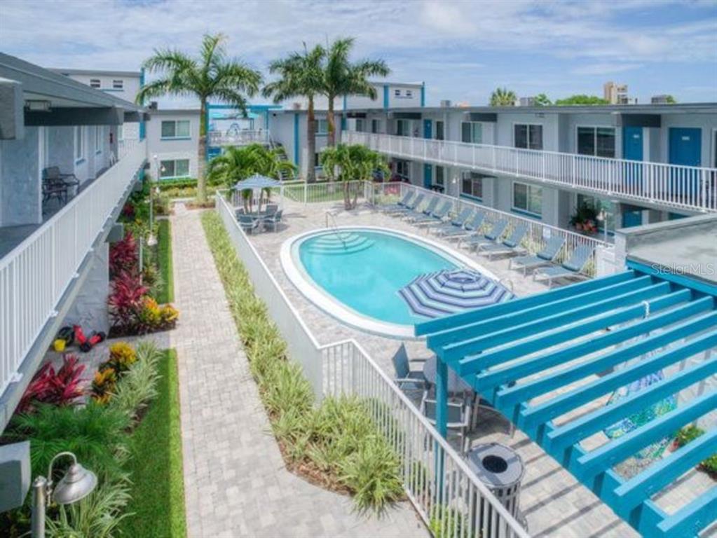 An elevated view of a motel courtyard featuring a swimming pool, lounge chairs, and palm trees — 1824 SHORE DRIVE S UNIT 201, SOUTH PASADENA, FL
