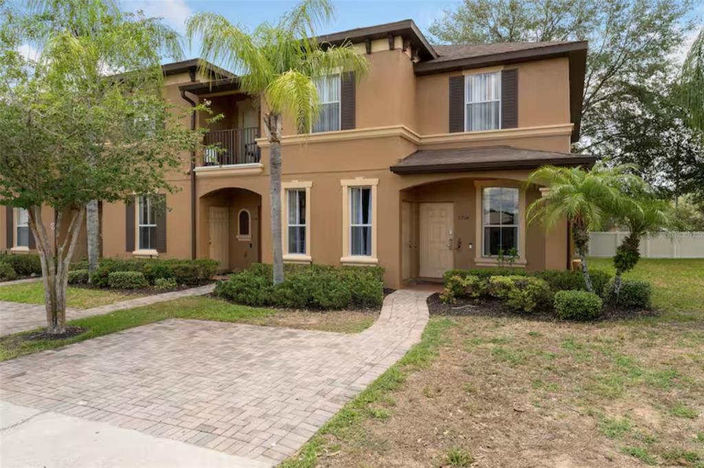 A two-story tan townhouse with a paved driveway, a small balcony, and landscaped front yard — 2204 CALABRIA AVENUE, DAVENPORT, FL