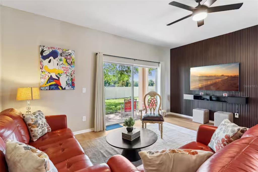 A living room features red leather sofas, a slatted wood accent wall, and sliding glass doors — 2204 CALABRIA AVENUE, DAVENPORT, FL