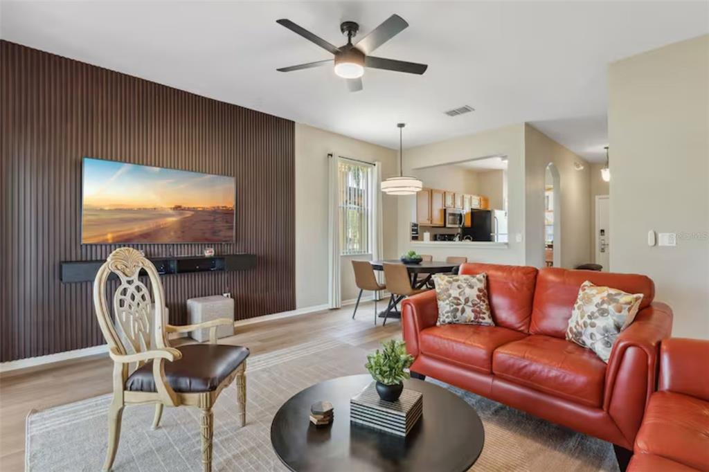 A living room features a slatted wood accent wall, a red sofa, and a ceiling fan — 2204 CALABRIA AVENUE, DAVENPORT, FL