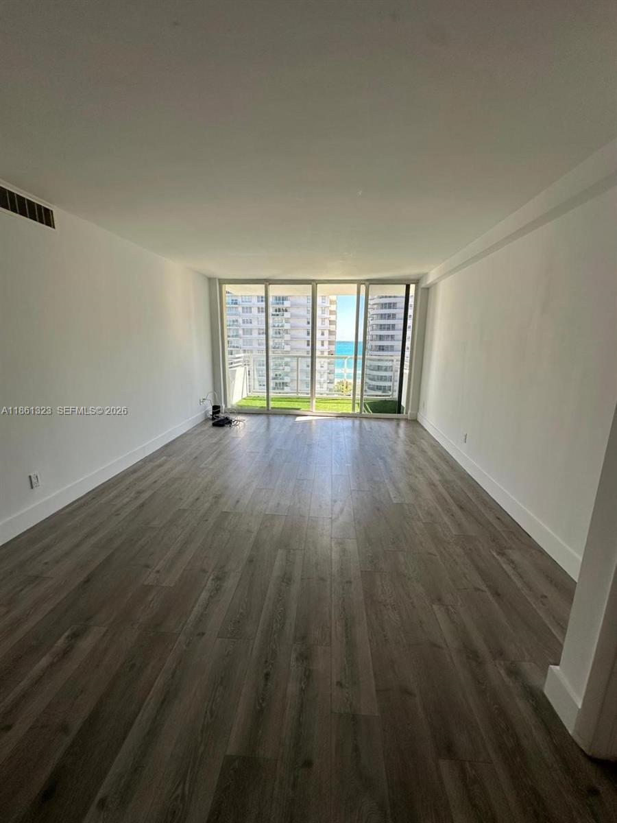 An empty room with light wood-look flooring features a large glass door leading to a balcony — 5600 Collins Ave # 11W, Miami Beach FL 33140, MIAMI BEACH, FL