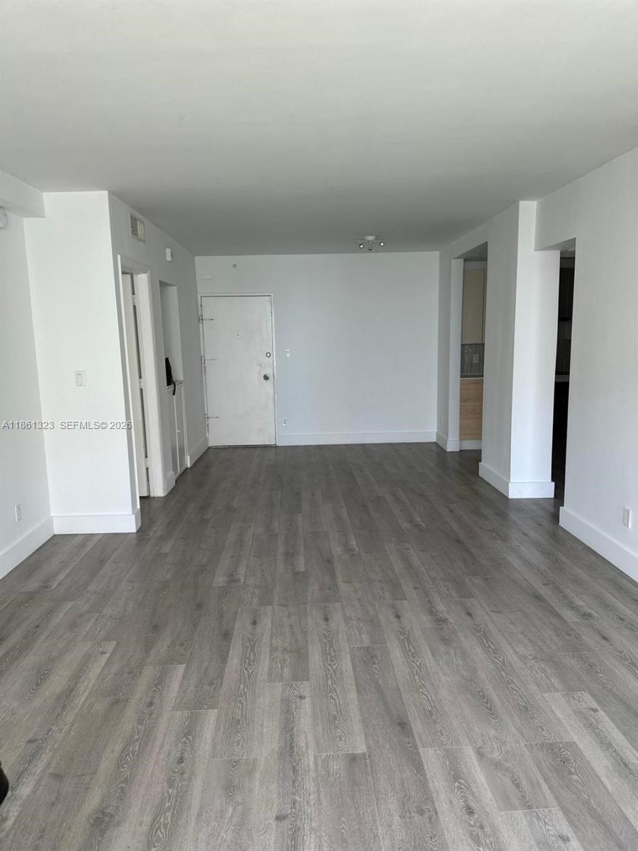 An empty room features gray wood-look flooring, white walls, and a white entry door — 5600 Collins Ave # 11W, Miami Beach FL 33140, MIAMI BEACH, FL