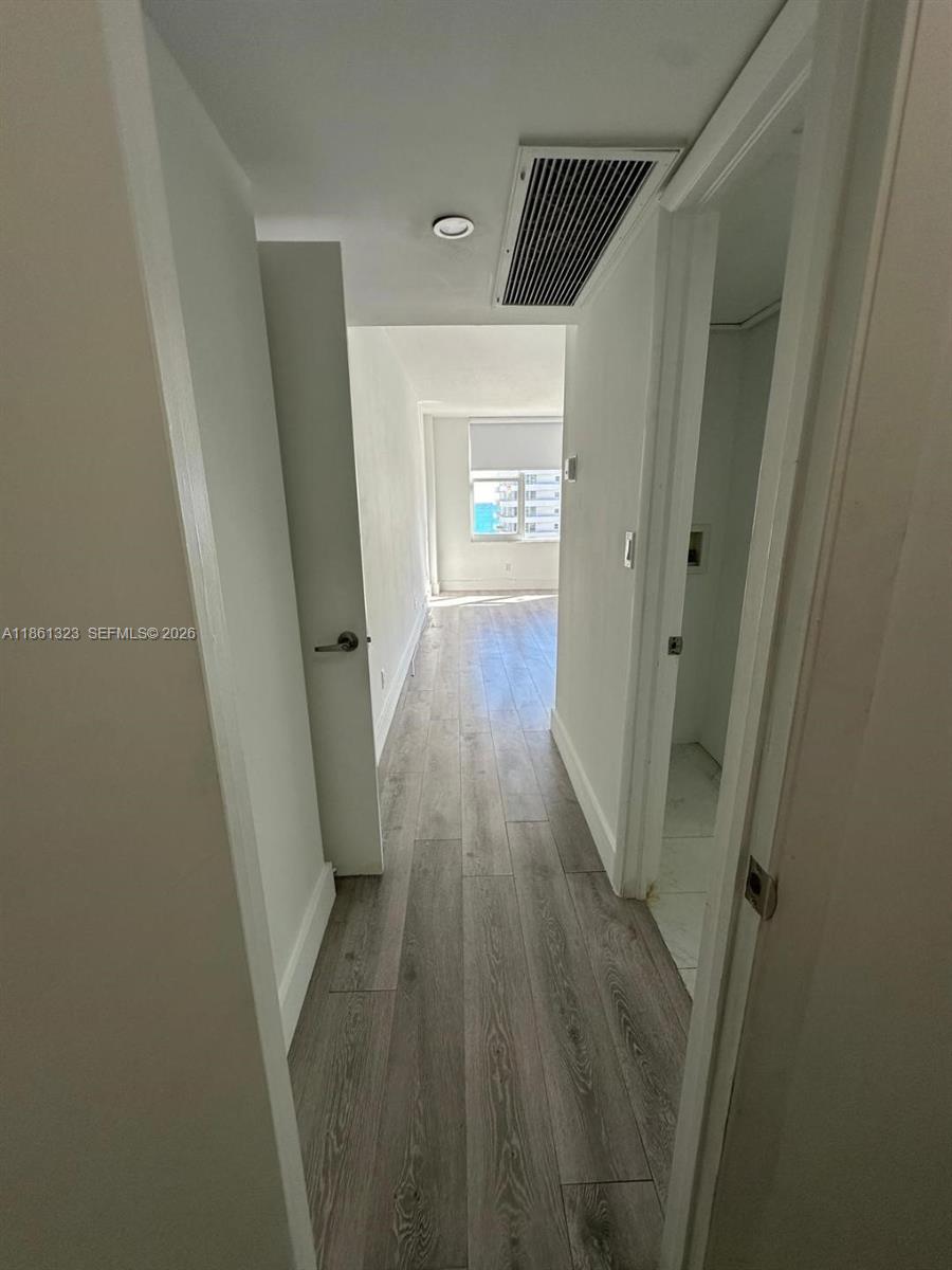 A hallway with wood-look flooring leads toward a windowed room with a view — 5600 Collins Ave # 11W, Miami Beach FL 33140, MIAMI BEACH, FL
