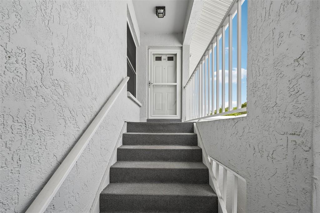A set of carpeted stairs leads up to a white front door on a landing — 1041 CAPRI ISLES BOULEVARD UNIT 209, VENICE, FL