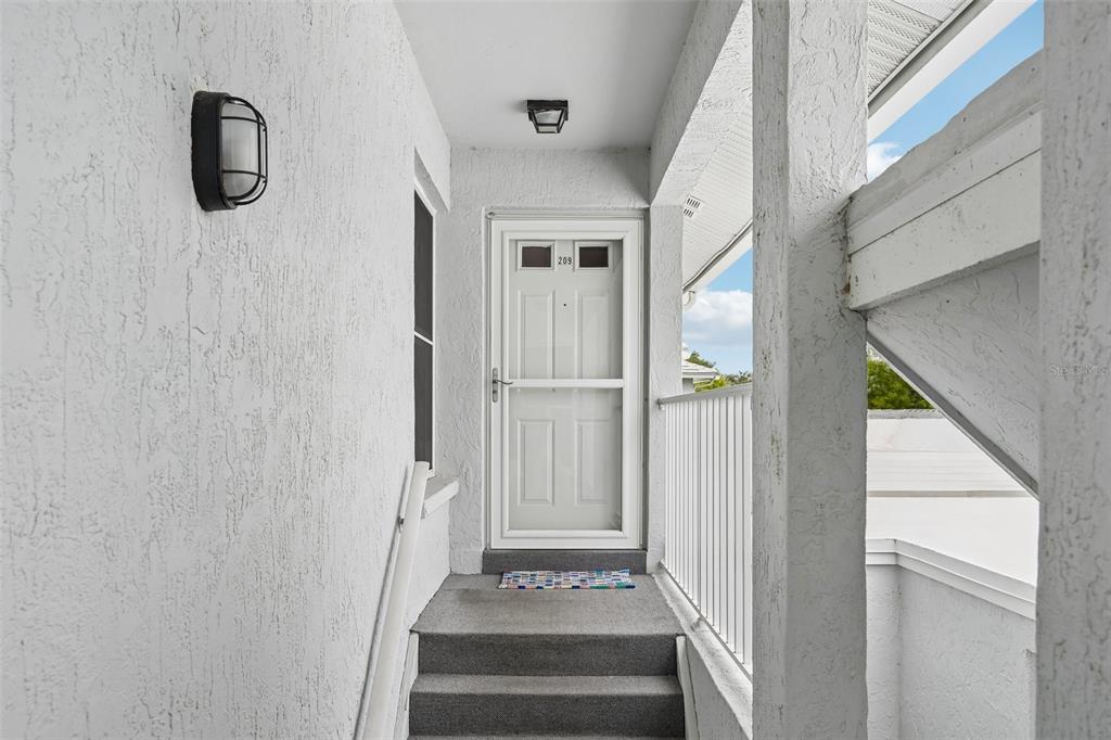 An exterior view of a residential unit entrance with stairs leading to a white door — 1041 CAPRI ISLES BOULEVARD UNIT 209, VENICE, FL