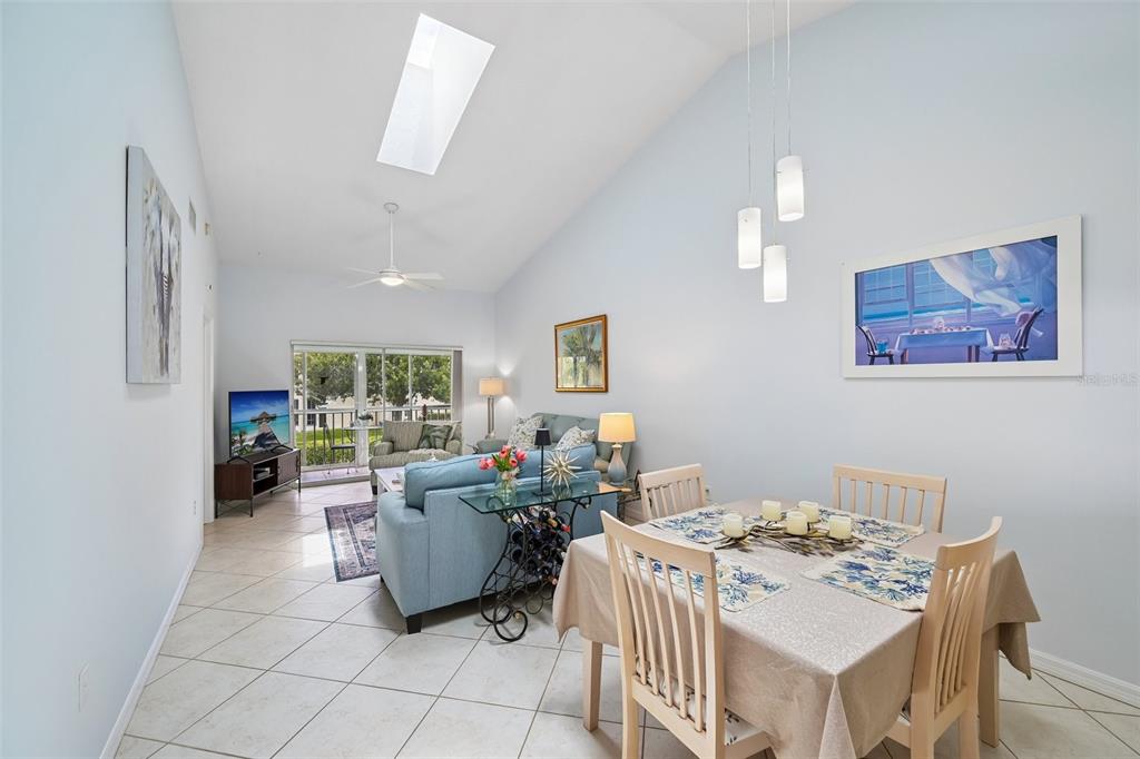 A dining area and living room with vaulted ceilings, tile floors, and a skylight — 1041 CAPRI ISLES BOULEVARD UNIT 209, VENICE, FL