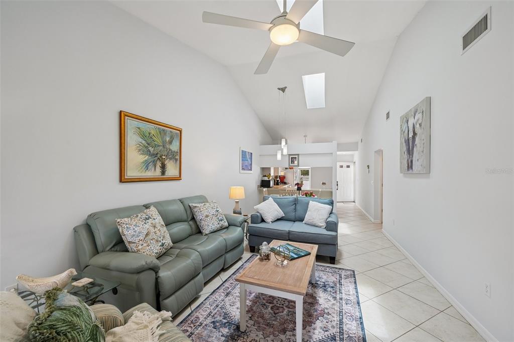 A living room features vaulted ceilings, tile flooring, a ceiling fan, and two sofas — 1041 CAPRI ISLES BOULEVARD UNIT 209, VENICE, FL